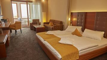 A hotel room with a large bed, a sofa, a desk, and a chair. There is a balcony with a view.