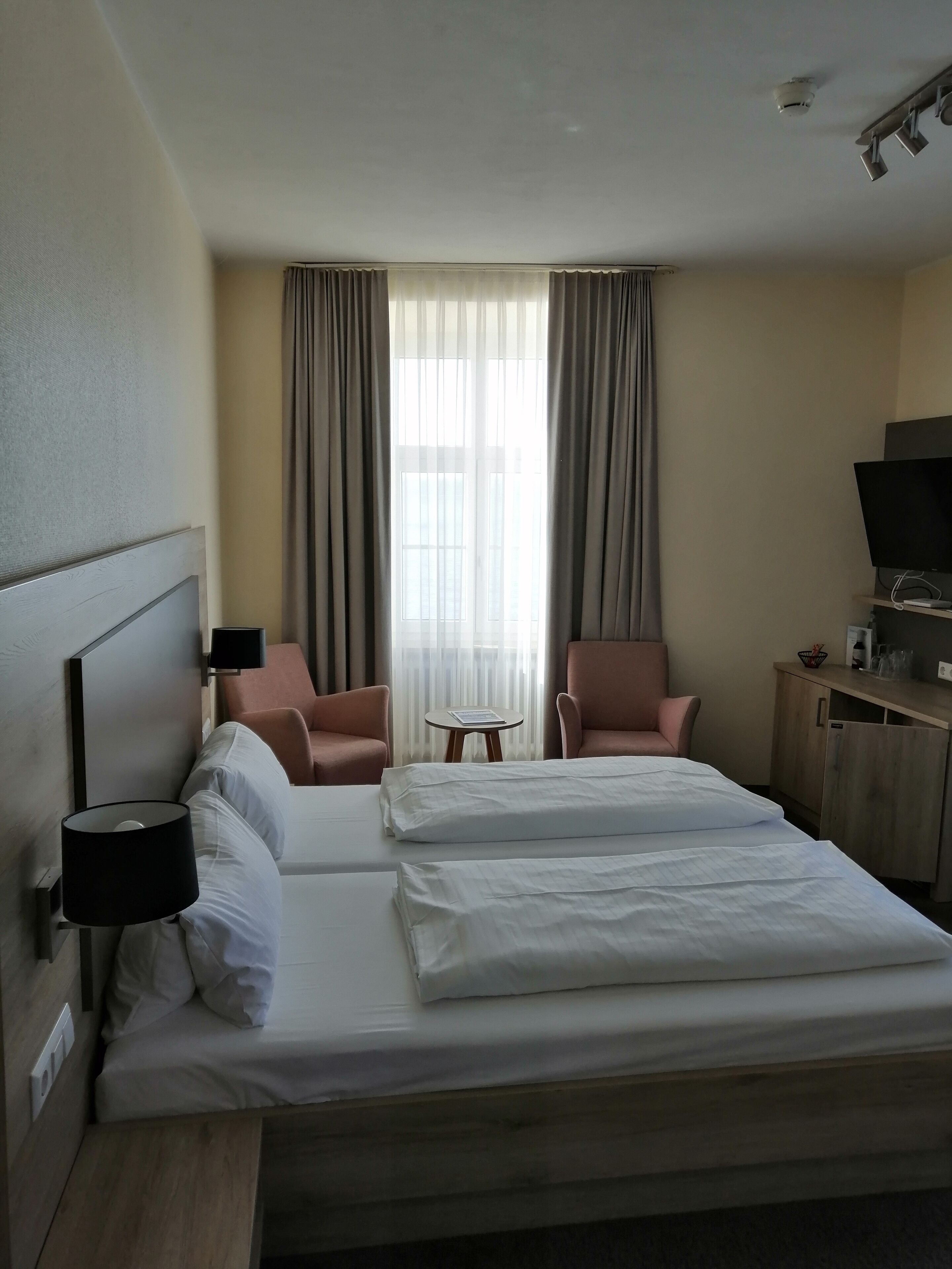 Ein Hotelzimmer mit einem großen Bett, zwei Sesseln, einem kleinen Tisch, einem Fernseher und einem Kleiderschrank.