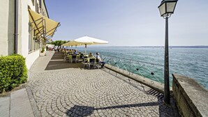 Un café situé au bord de l’eau, avec une terrasse et des places assises à l’extérieur, un patio pavé et une vue sur la mer.
