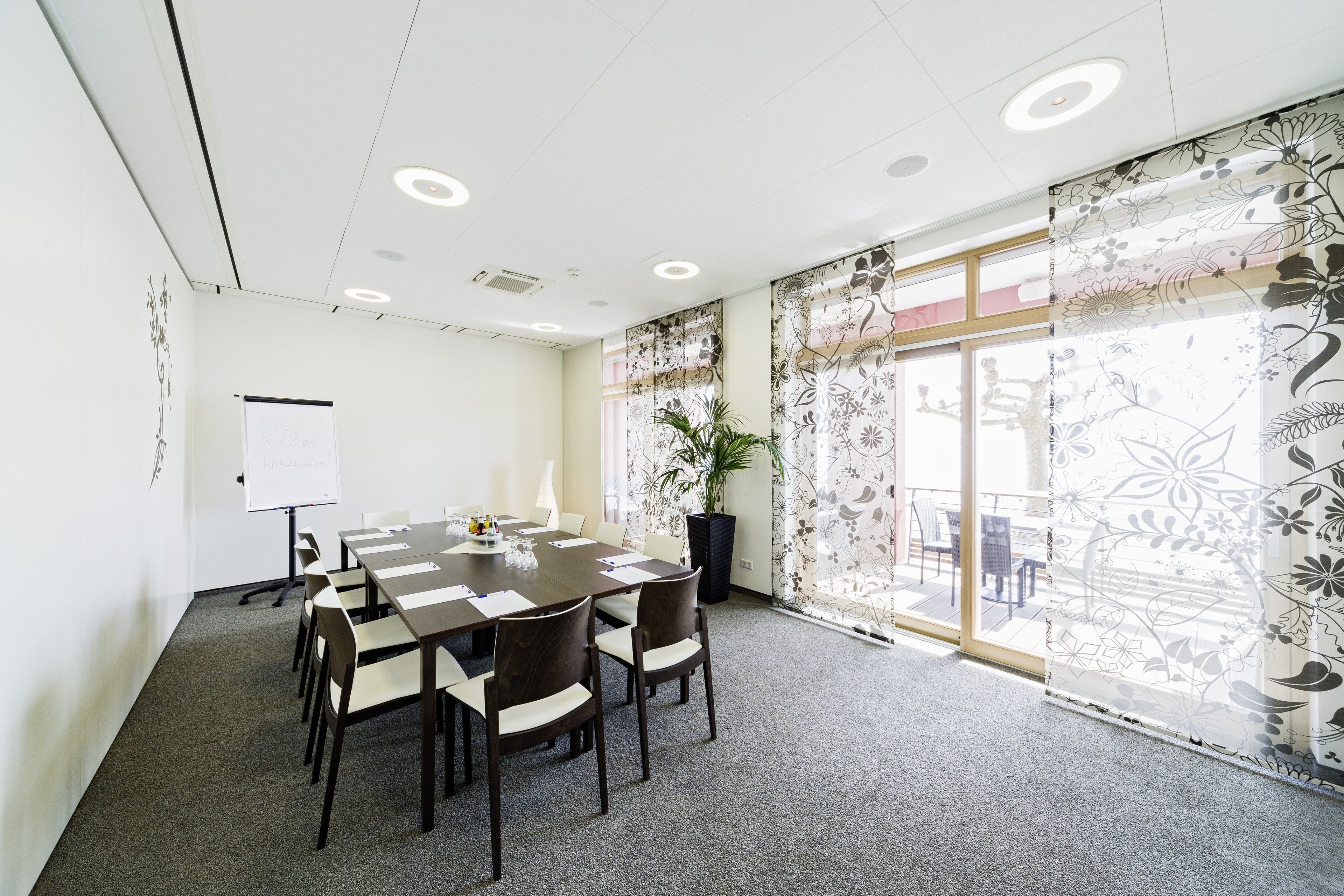 A conference room with a large table, chairs, a whiteboard, and a potted plant.