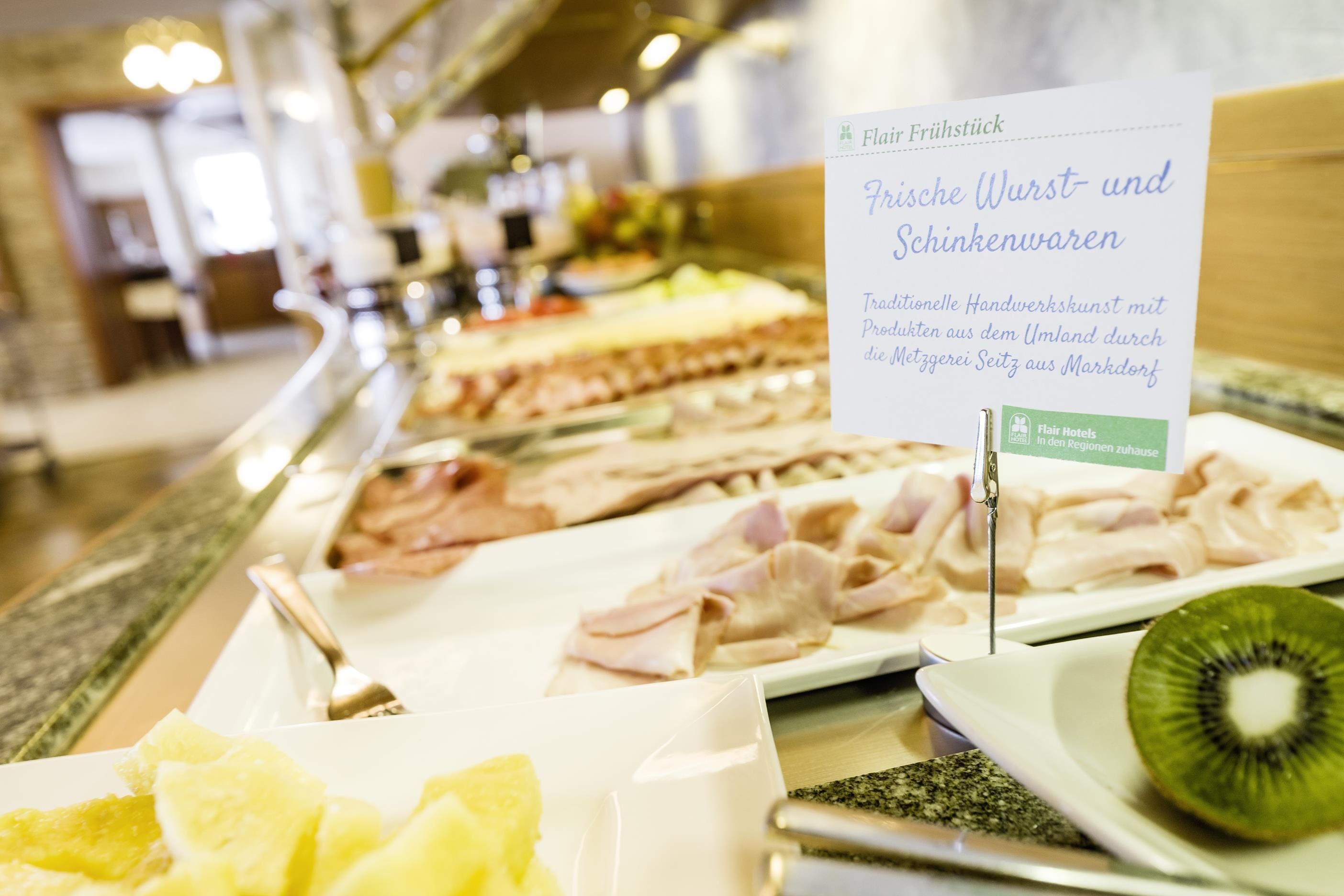 A buffet table with various food items including sliced meats, fruits, and a sign indicating traditional handcrafts from Markdorf.