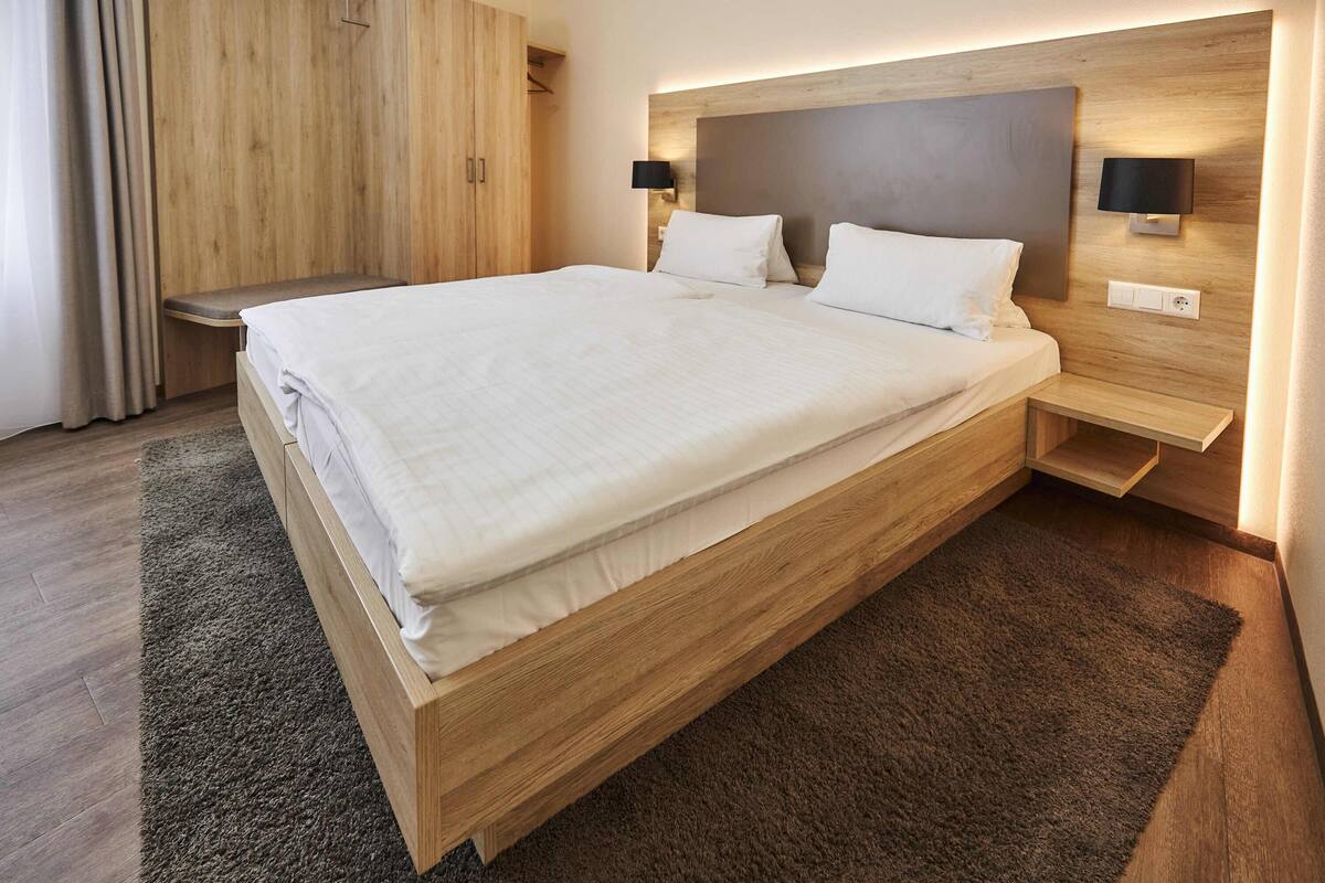 Een moderne hotelkamer met een groot bed, een houten hoofdeinde, nachtkastjes en een inbouwkast.