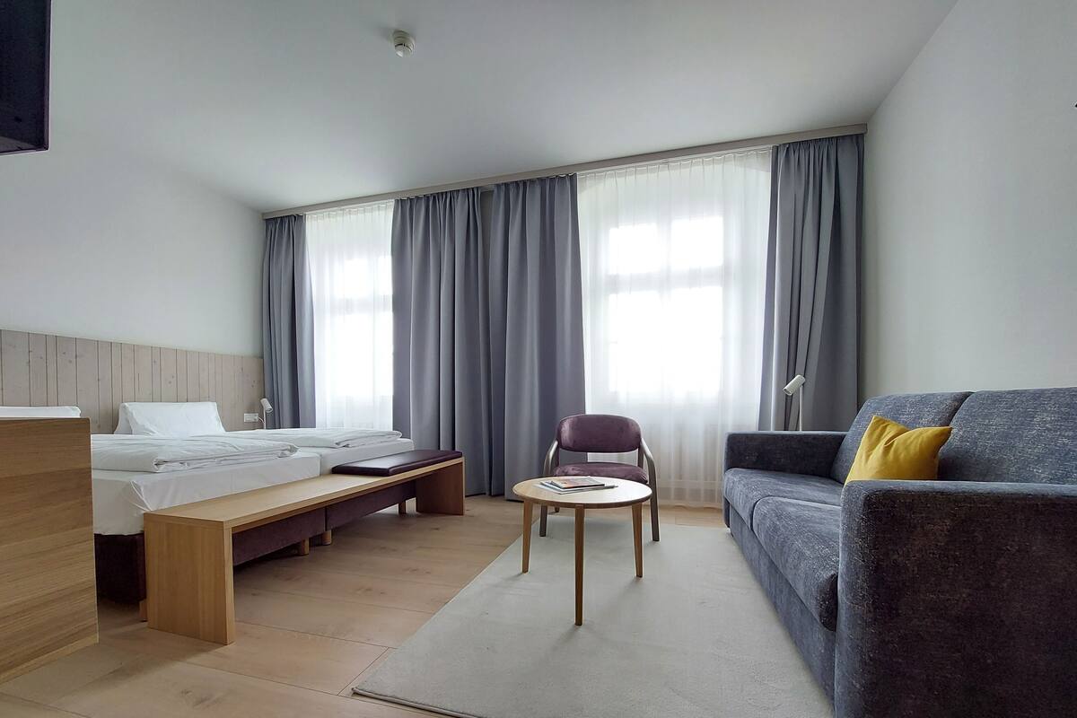 Een hotelkamer met een bed, een bank, een stoel, een bijzettafeltje en een raam met gordijnen.