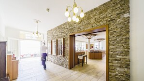 Un hall d’hôtel spacieux, agrémenté d’un mur en pierre, d’un comptoir d’accueil en bois et d’un lustre.