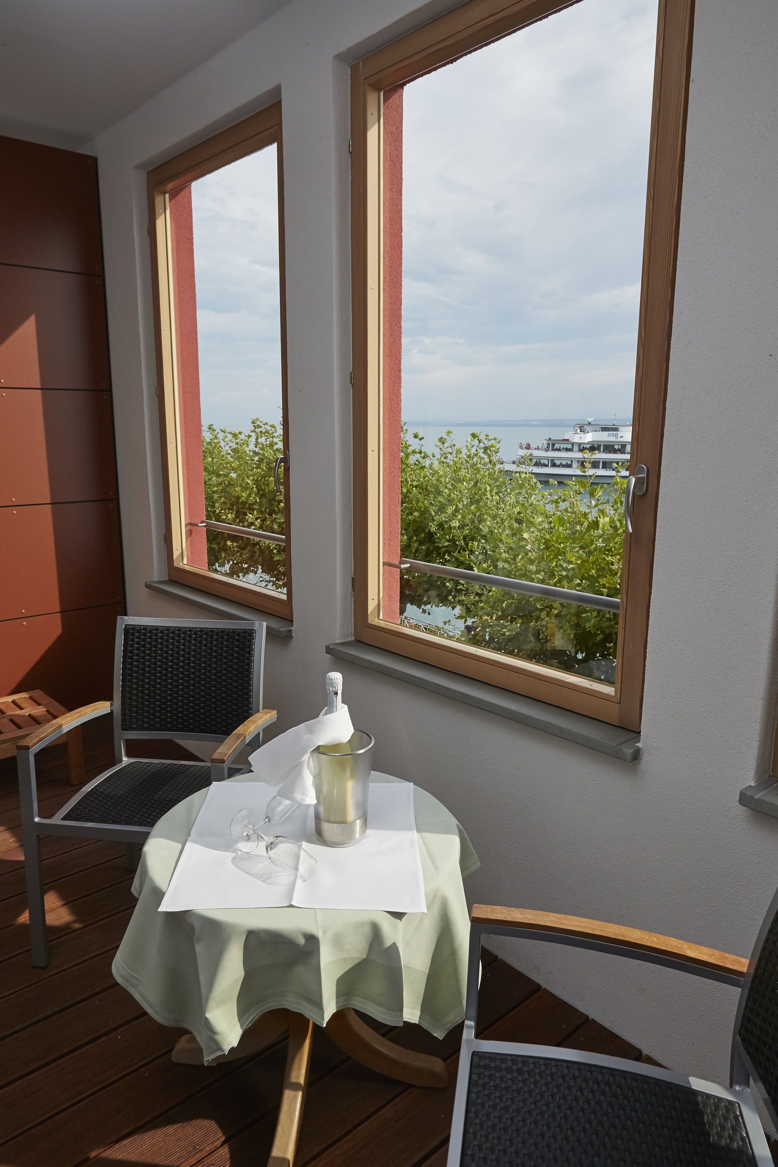 A balcony with a table set for two, overlooking a body of water and greenery.