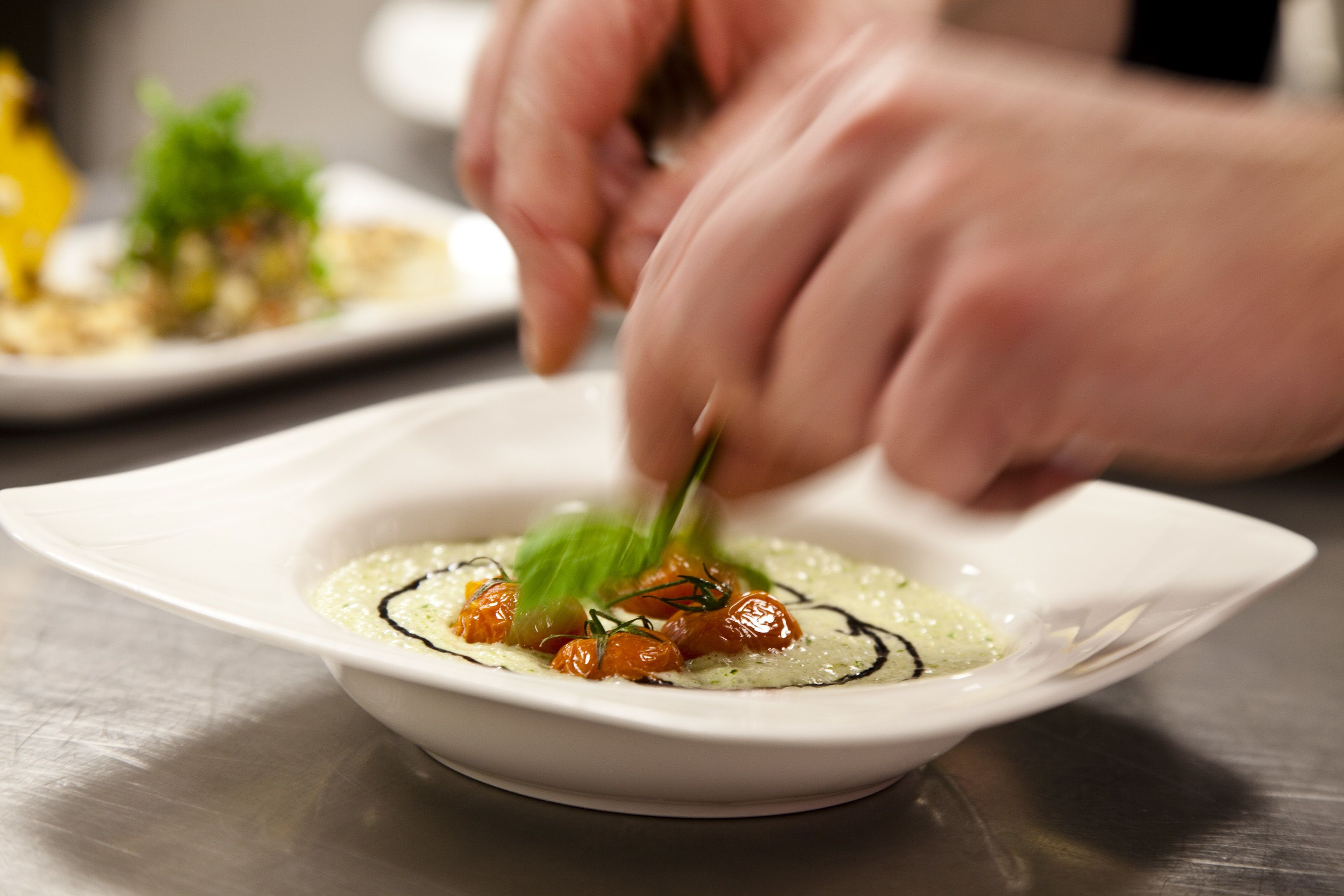 A chef preparing a dish with a white plate and a spoon.