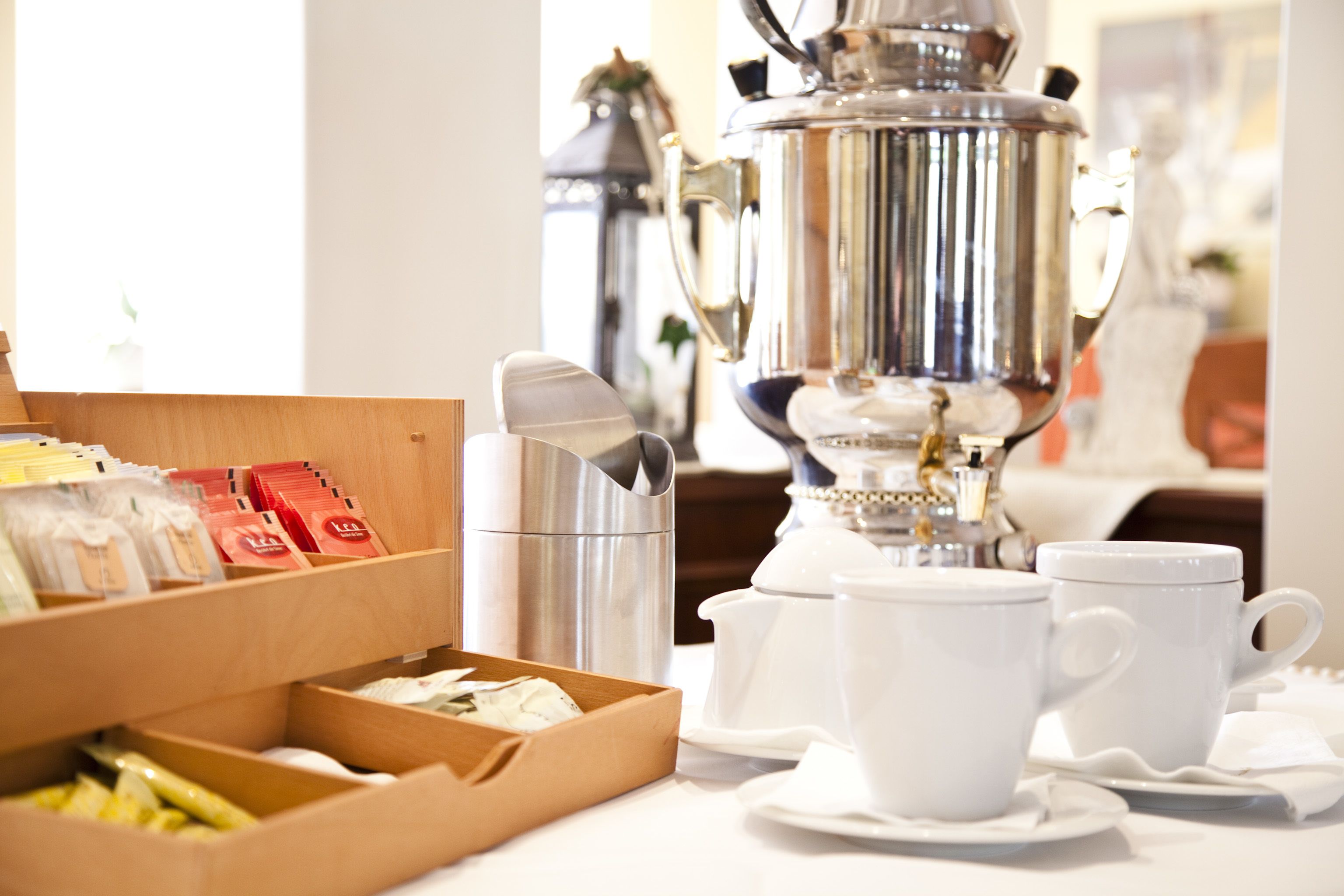 A breakfast setup with a silver coffee pot, white cups, and a box of tea packets.