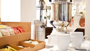 A breakfast setup with a silver coffee pot, white cups, and a box of tea packets.
