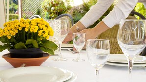 Una mesa dispuesta con platos blancos, copas de vino transparentes y un arreglo floral amarillo en maceta.
