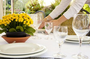 Uma mesa posta com pratos brancos, copos de vinho transparentes e um arranjo de flores amarelas em vaso.