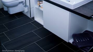 A modern bathroom with a white sink, a mirror, and a toilet.