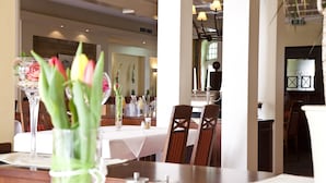 Un comedor con mesas dispuestas para el servicio, sillas y un jarrón de flores sobre la mesa.
