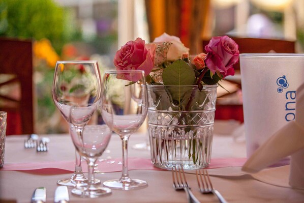 A table set with wine glasses, a vase with pink roses, and a white mug with a logo.