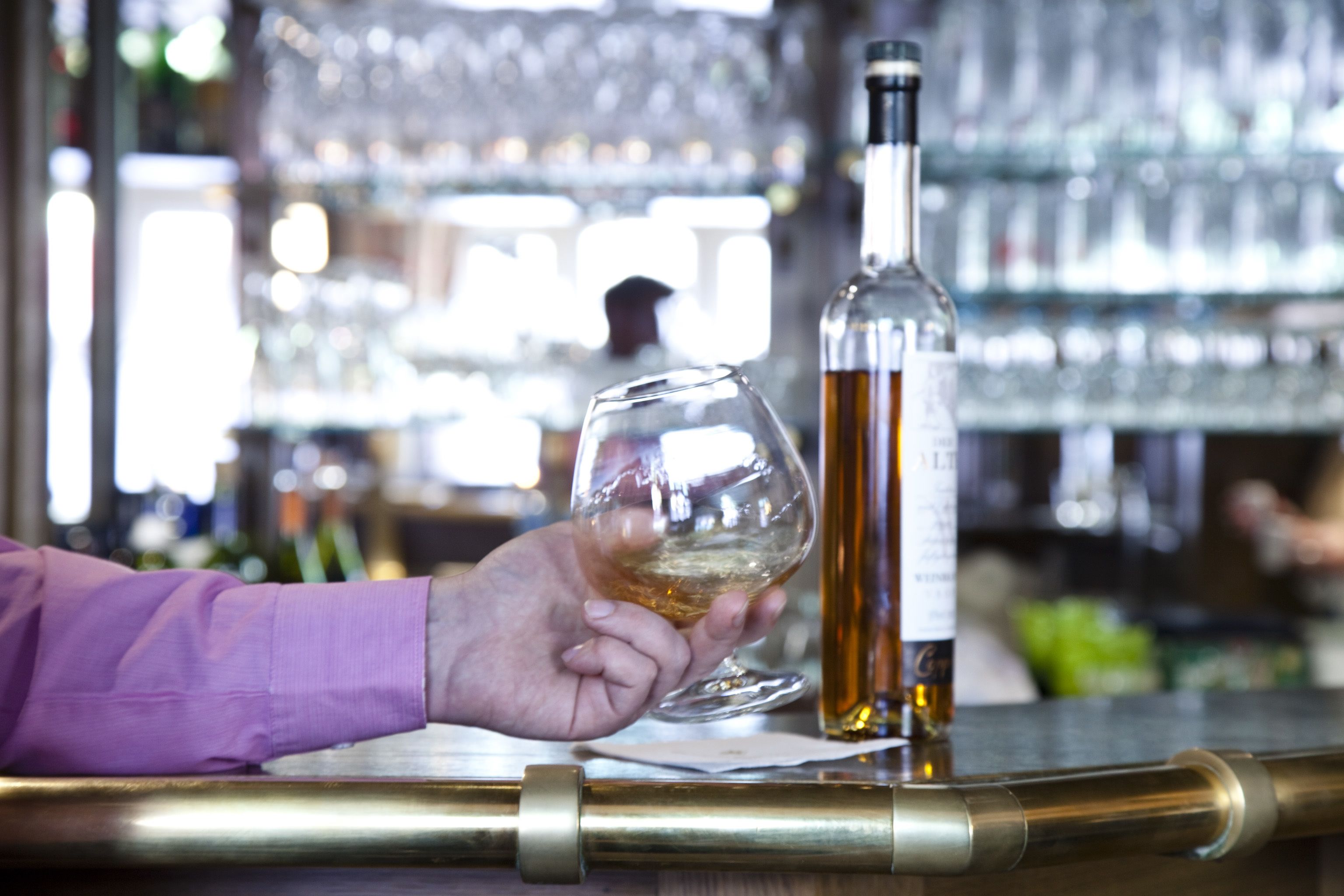 Une main tenant un verre à vin à côté d’une bouteille sur le comptoir d’un bar.