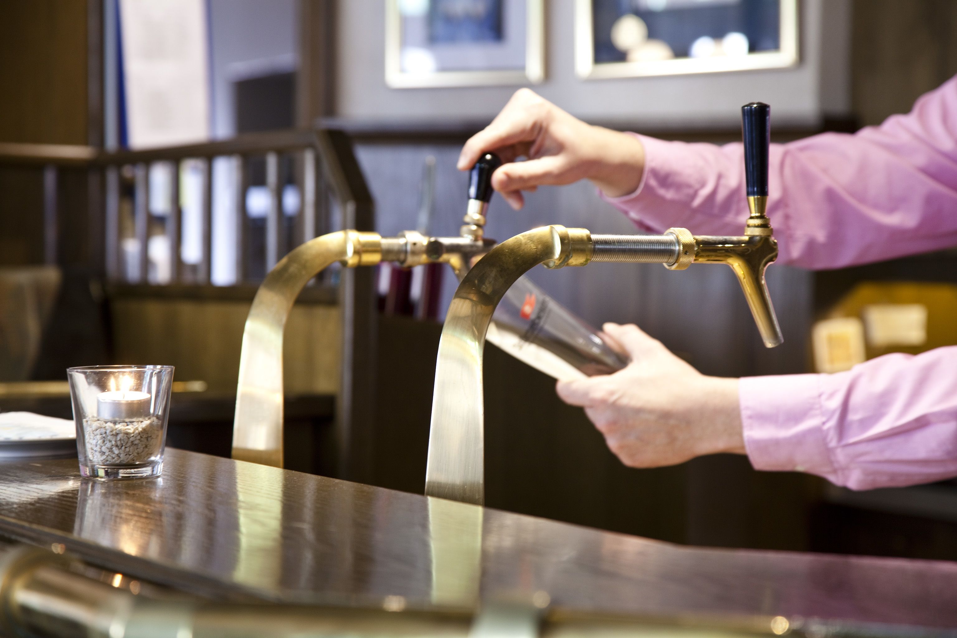 A person pouring beer from a tap into a glass on a bar counter.