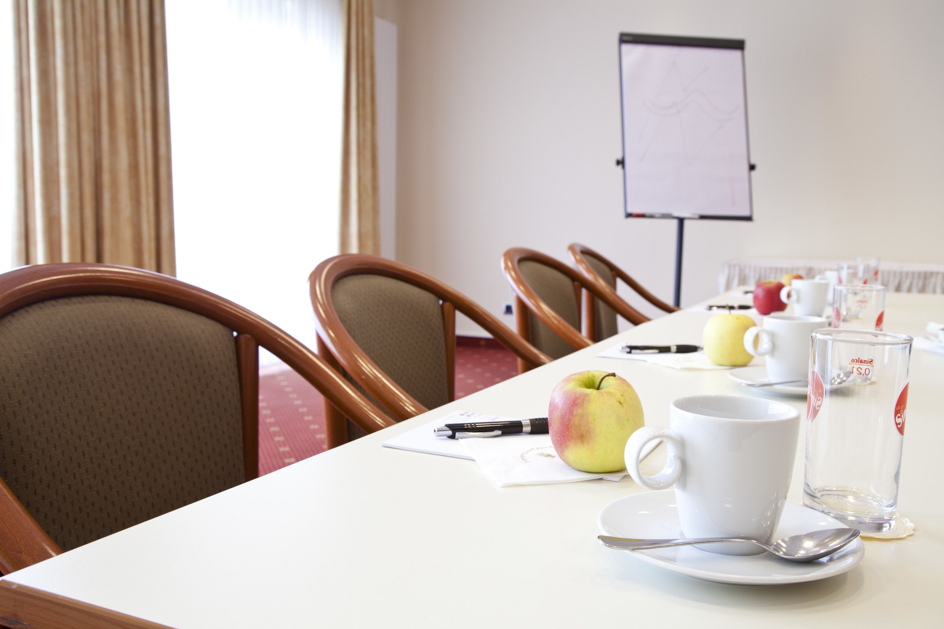 A conference room with a white table, wooden chairs, a whiteboard, and a glass of water on the table.
