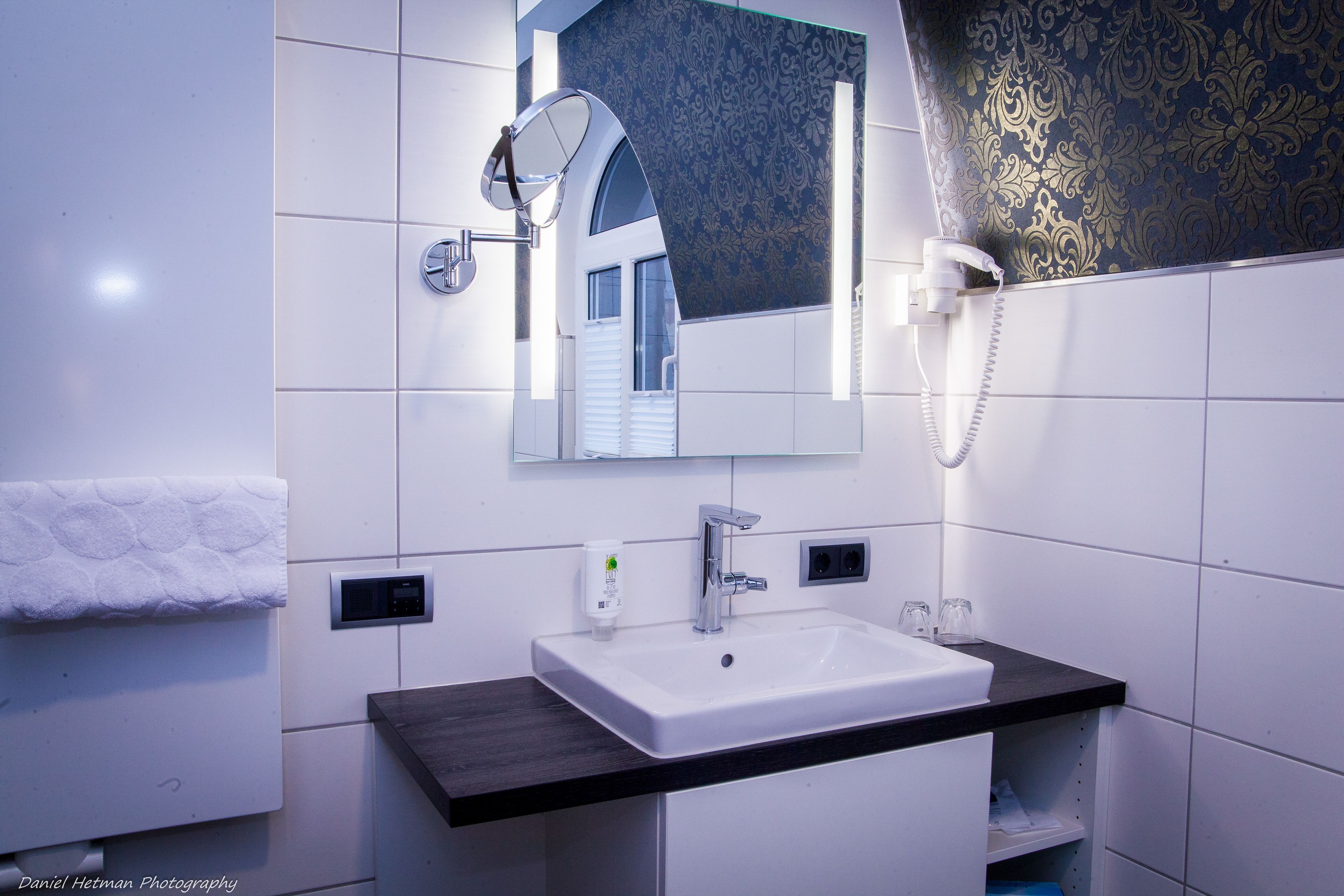 Un baño moderno con lavamanos blanco, encimera oscura y un espejo grande.