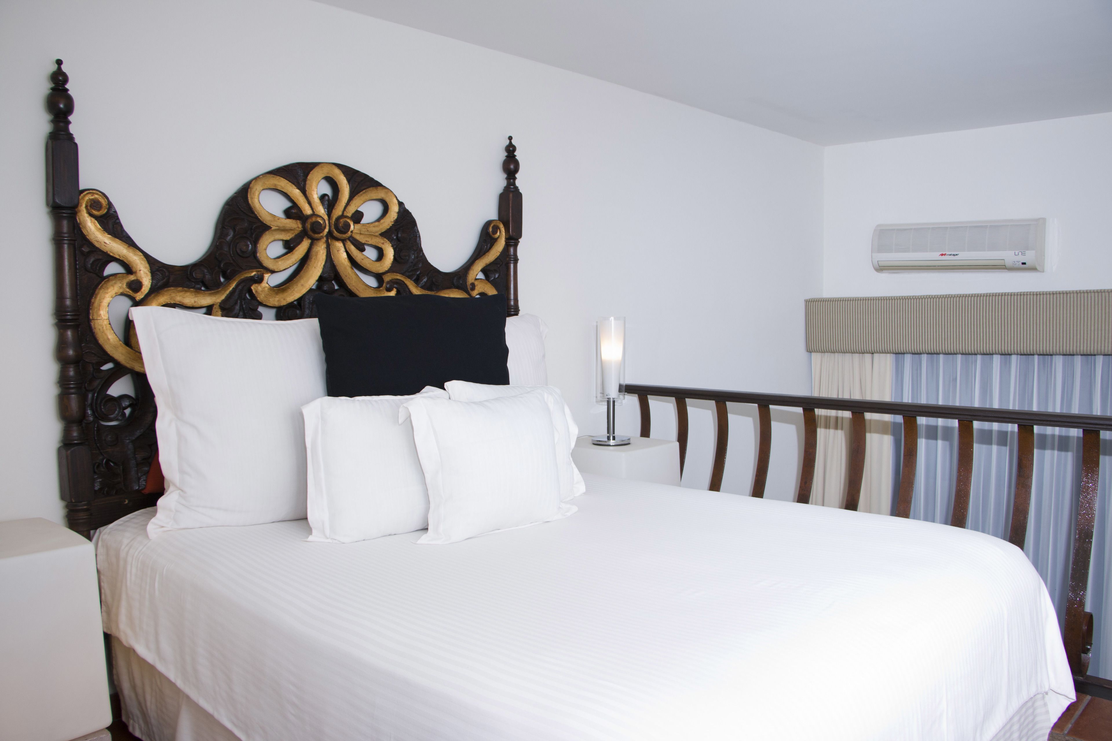 A neatly made bed with a wooden headboard, a bedside table with a lamp, and a window with curtains.