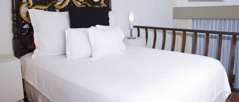 A neatly made bed with a wooden headboard, a bedside table with a lamp, and a window with curtains.