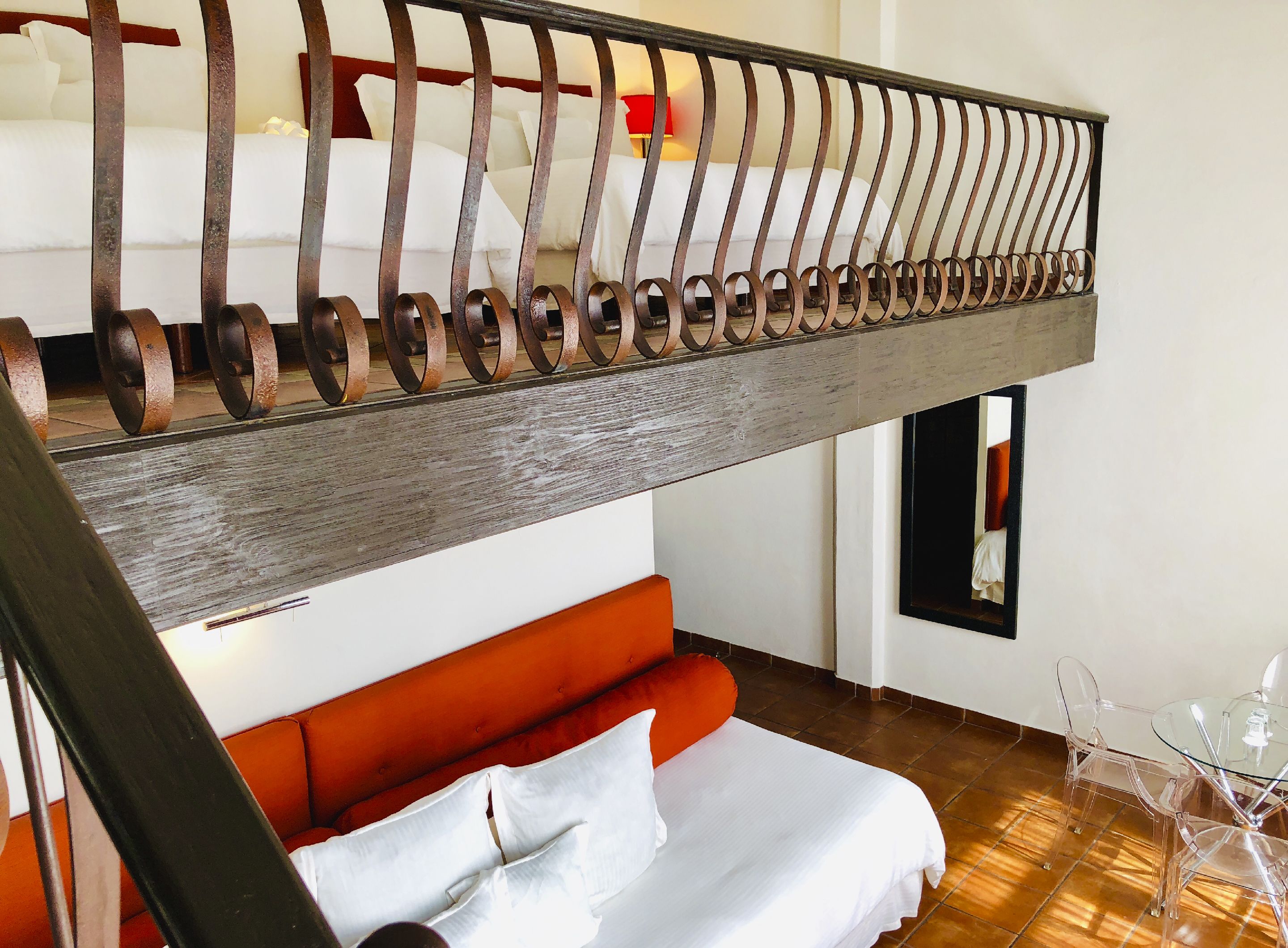 Una habitación de hotel moderna con una escalera de madera, un sofá rojo, una mesa de vidrio y una cama con ropa blanca.