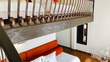 Una habitación de hotel moderna con una escalera de madera, un sofá rojo, una mesa de vidrio y una cama con ropa blanca.
