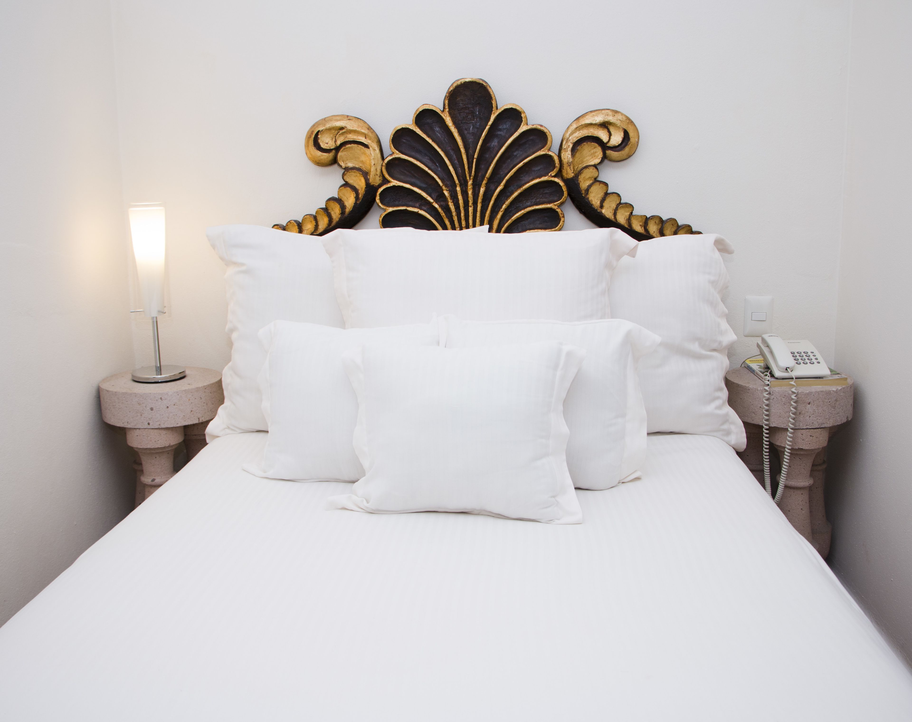A bed with white bedding, a decorative headboard, a bedside lamp, and a telephone on a nightstand.