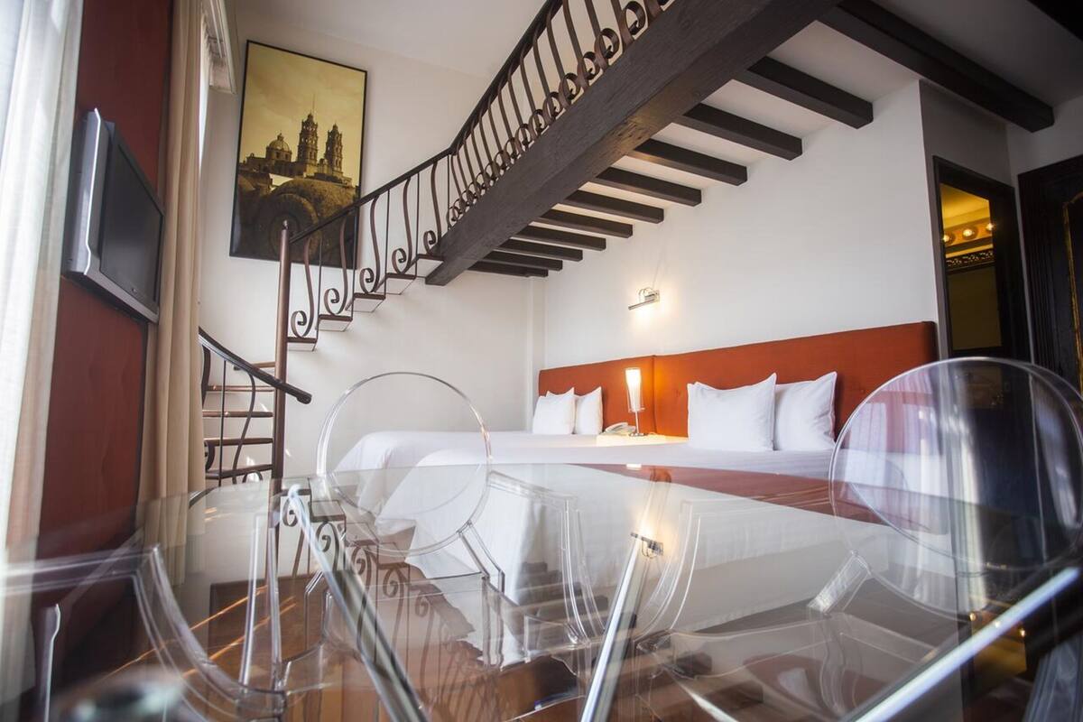 A hotel room with a large bed, a wooden staircase, and a cityscape painting on the wall.