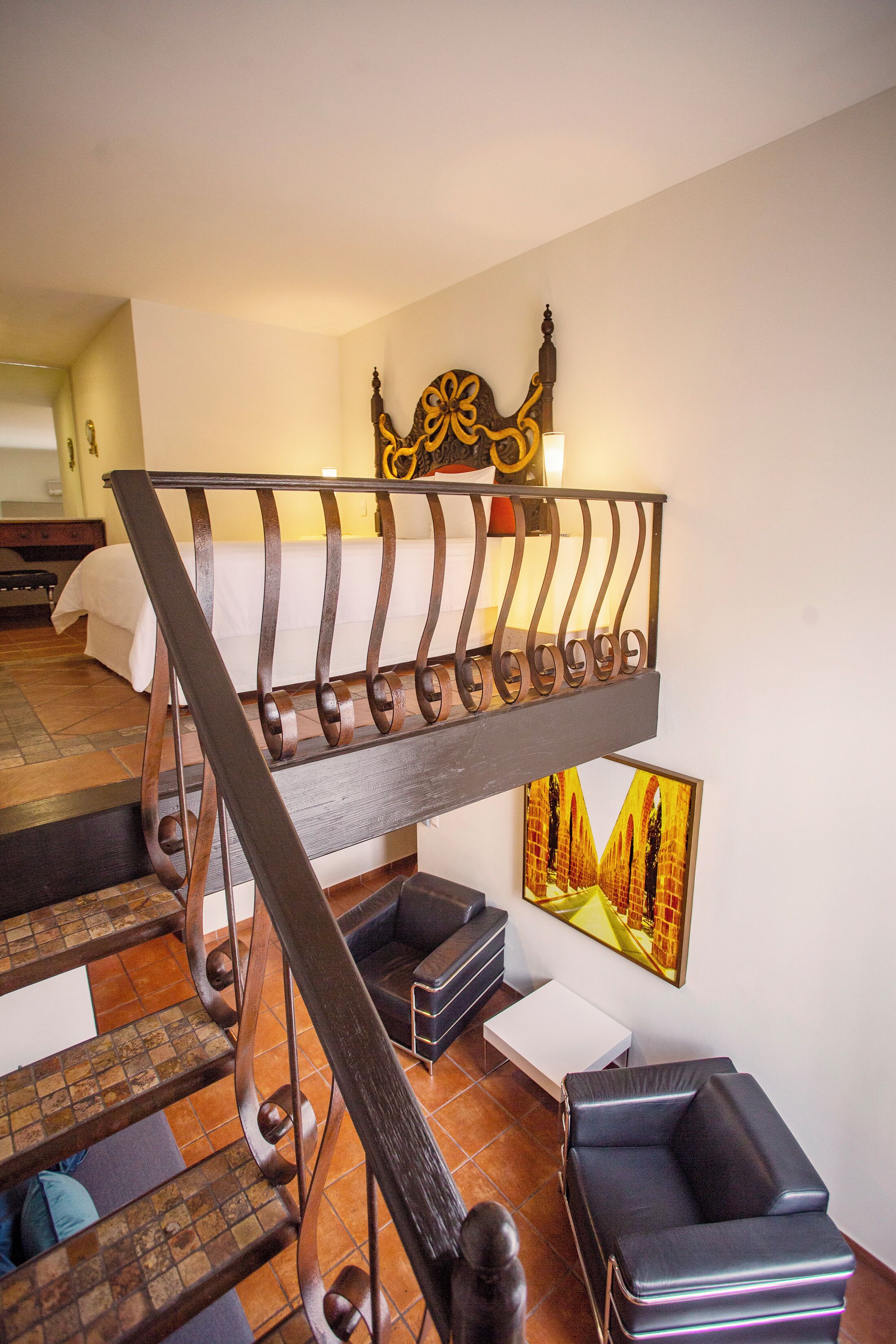 A staircase with a wrought iron railing leading to a bedroom with a bed and a painting on the wall.