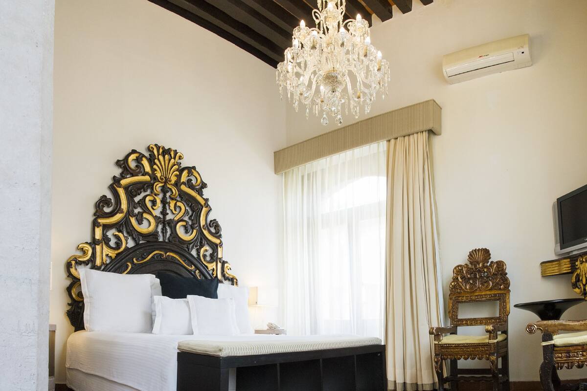 A bedroom with a large ornate bed, a chandelier, an air conditioning unit, and a television.