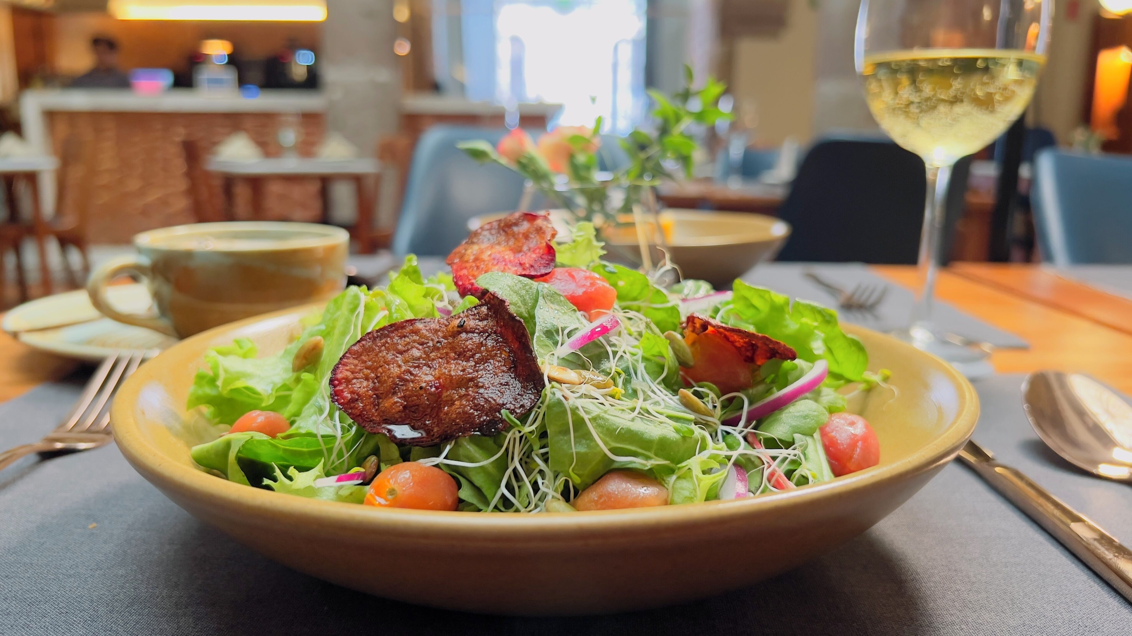 A bowl of salad with various vegetables and a piece of meat on a table.