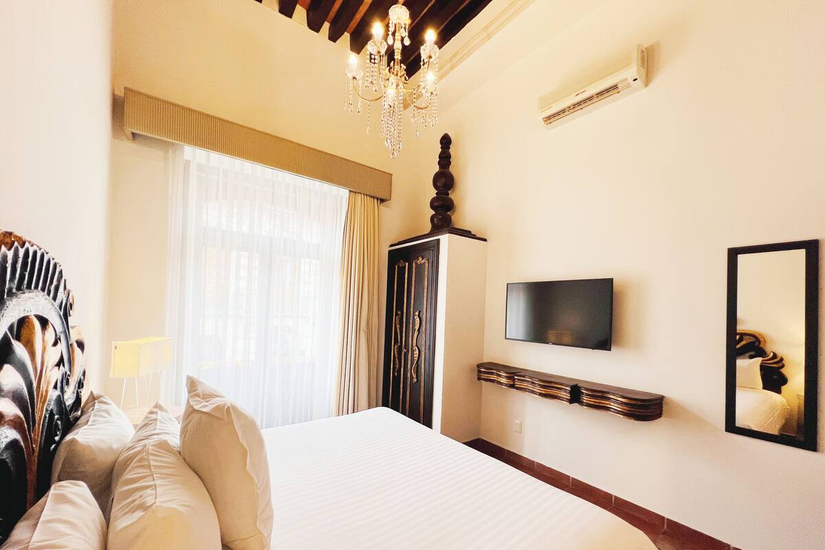 A hotel room with a large bed, a television, a mirror, and a chandelier.