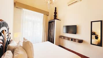 Quarto de hotel com uma cama grande, televisão, espelho e lustre.