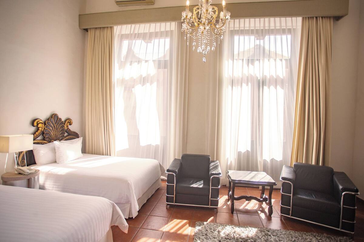 A hotel room with two beds, a chandelier, and a table with chairs.
