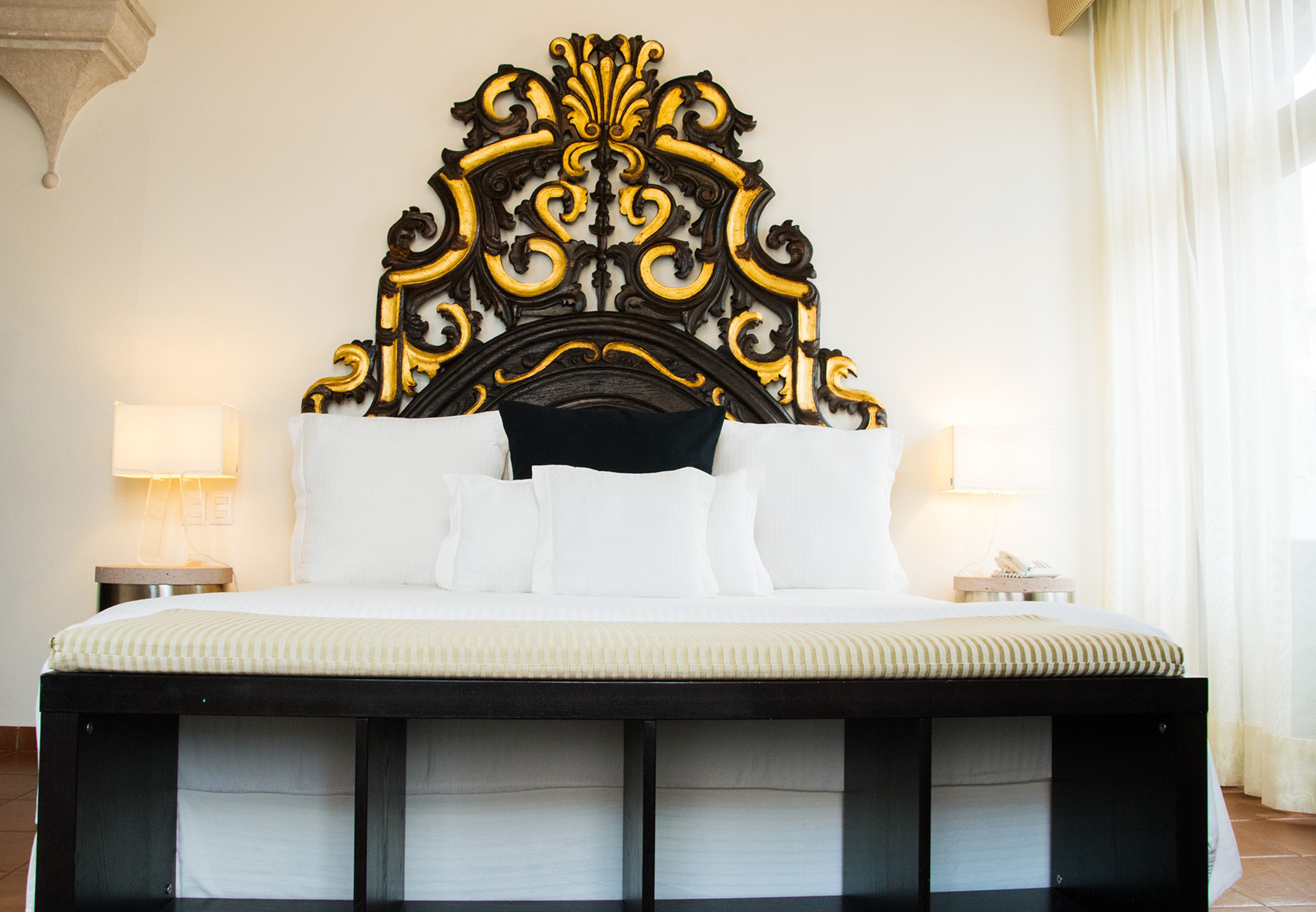 A large bed with a black and gold ornate headboard, white bedding, and two bedside lamps.