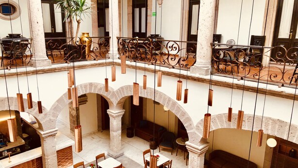 A spacious atrium with high ceilings, featuring a central open area with tables and chairs, surrounded by arches and columns. - HERENCIA By Hosting House (Morelia)