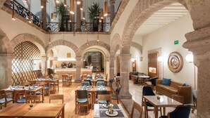 A spacious dining area with wooden tables and chairs, a central bar, and arched stone walls. - HERENCIA By Hosting House (Morelia)
