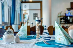 A dining table set with a clear glass vase, a salt and pepper shaker, a striped napkin holder, and a decorative sailboat. - Hotel Paulin (Trier)