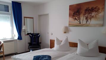 Habitación de hotel con cama, escritorio, silla, ventana con cortinas, un cuadro y una lámpara.