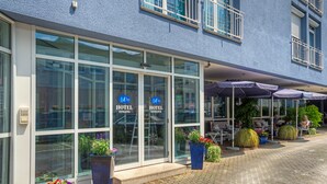 A hotel entrance with large glass doors, outdoor seating, and potted plants. - Hotel Paulin (Trier)
