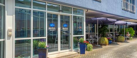 A hotel entrance with large glass doors, outdoor seating, and potted plants.