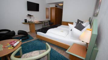 A hotel room with a bed, a desk, a chair, a TV, and a lamp.