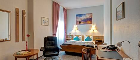 A hotel room with a bed, a desk, a chair, a desk lamp, and a painting on the wall.