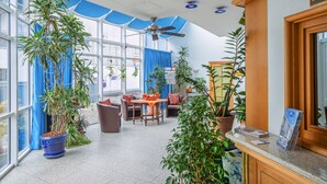 A spacious indoor area with large windows, ceiling fans, and multiple seating arrangements. - Hotel Paulin (Trier)