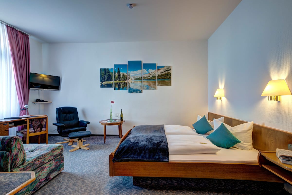 A hotel room with a bed, a desk, a chair, a TV, and a wall-mounted artwork.