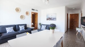 A modern living room with a dark blue sofa, white coffee table, and a large window. - Bahia (Santa Eulalia del Rio)
