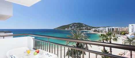 A balcony with a table set for breakfast overlooking a beach and the sea.