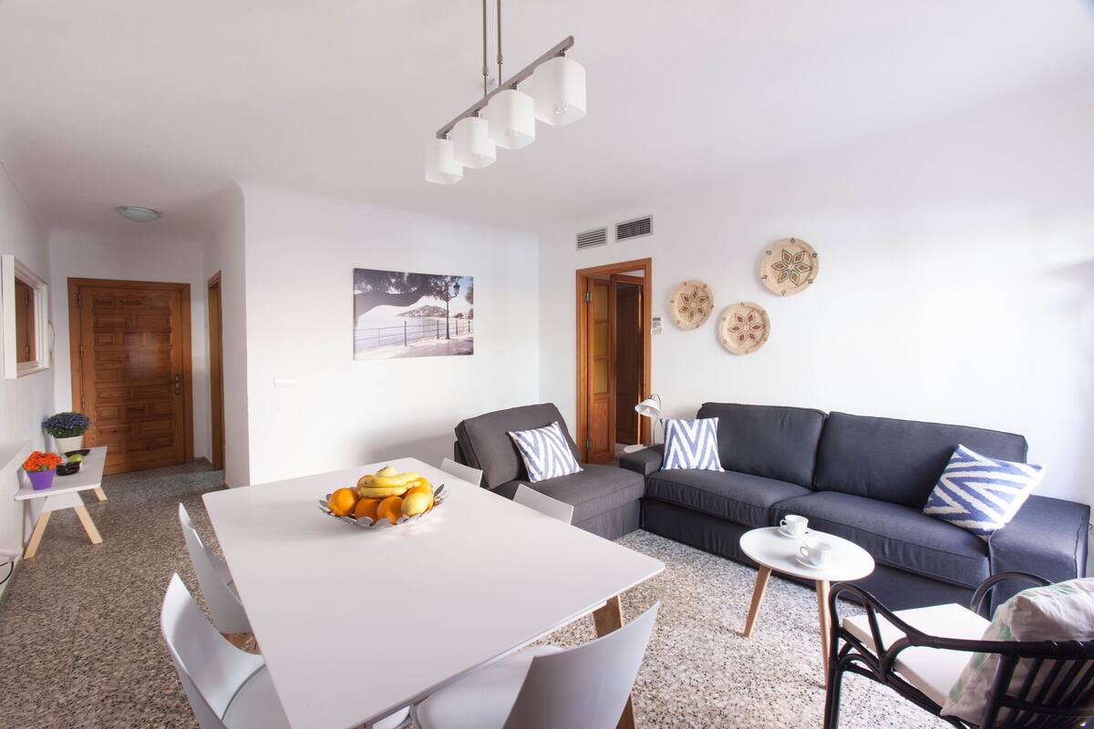 A modern living room with a white dining table, grey sofa, and a small round table with a cup and saucer.