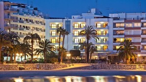 A beachfront hotel with multiple floors, palm trees, and a stone wall in the foreground. - Bahia (Santa Eulalia del Rio)