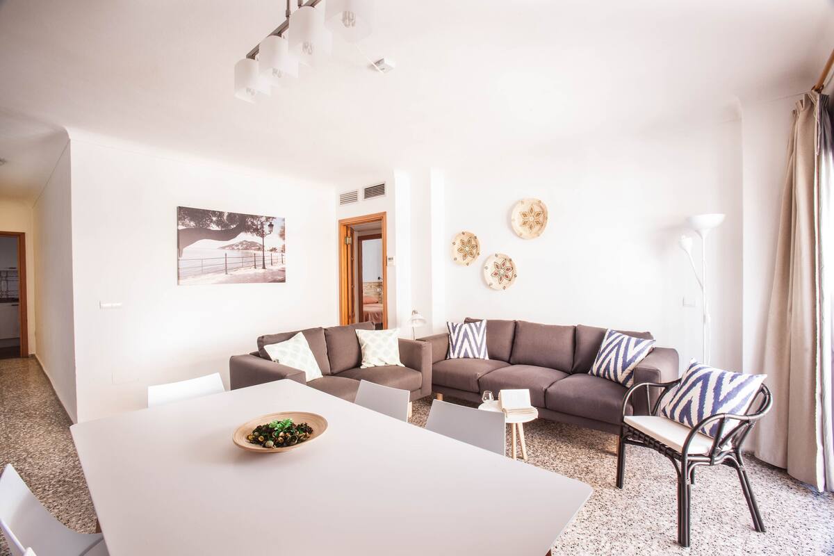A modern living room with a white dining table, two sofas, and a small side table.