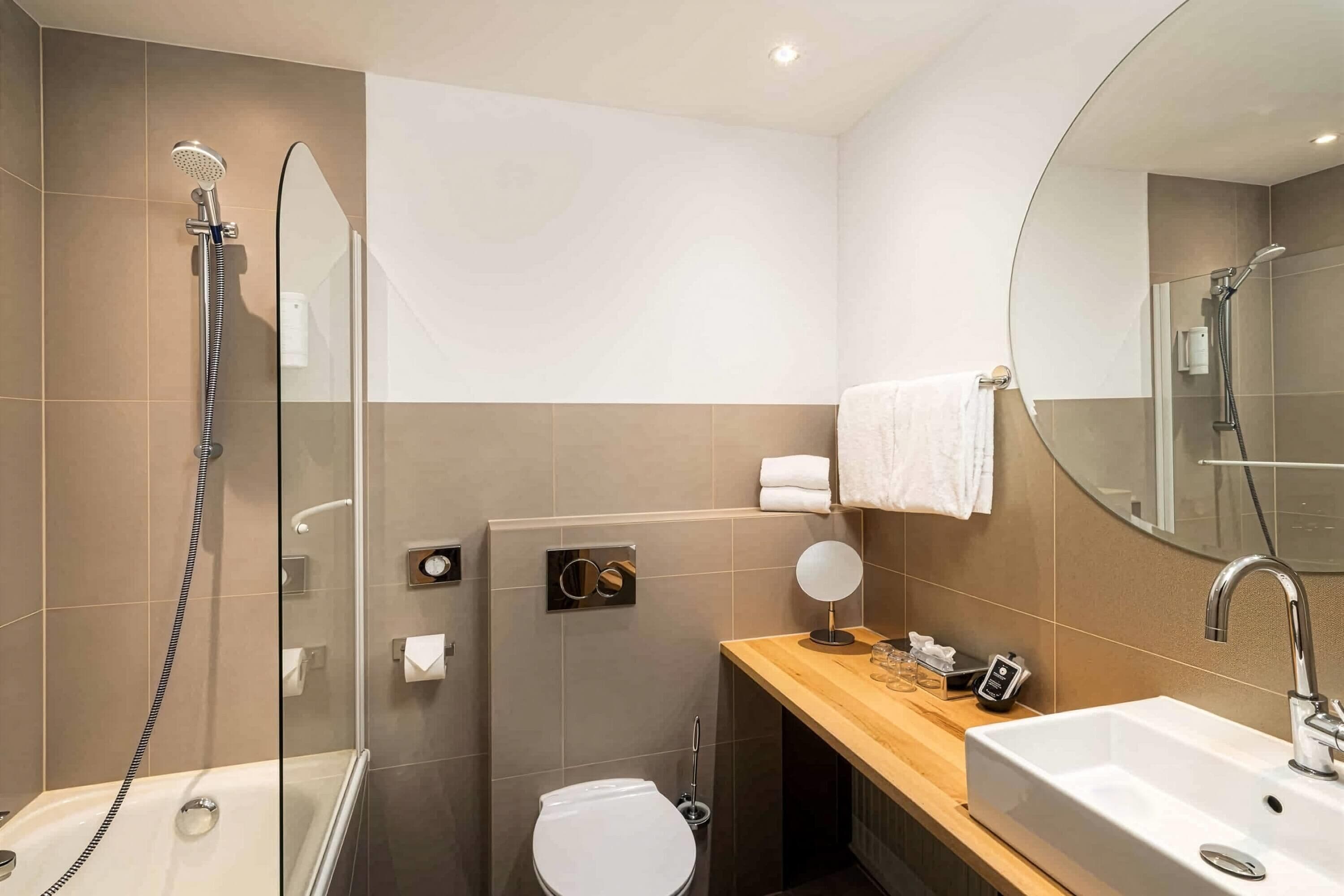 Un baño moderno con ducha acristalada, inodoro, lavabo con espejo y toallero.